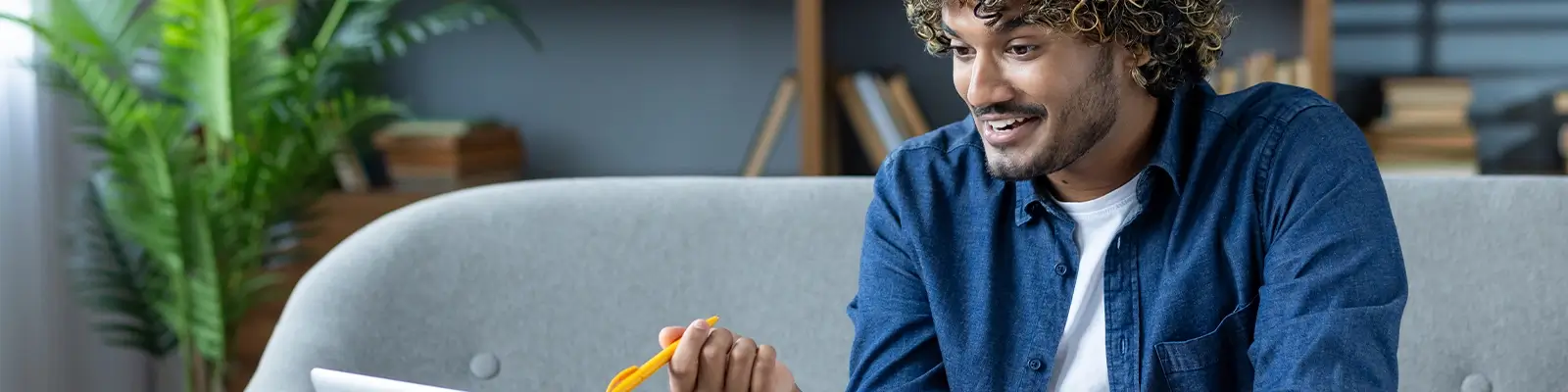Man speaking and gesturing with a pen in front of a laptop.
