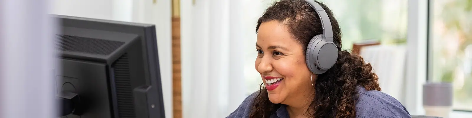 Woman wearing headphones and smiling in front of a computer.