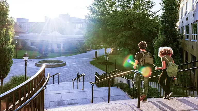 Two students walking down stairs on a university campus as the sun shines towards them